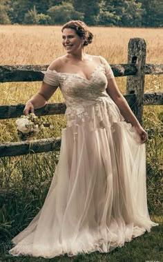 a woman standing in front of a wooden fence wearing a dress with flowers on it