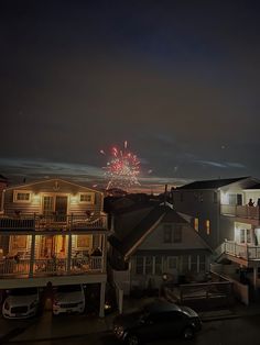 fireworks are lit up in the night sky over houses and parked cars on a city street