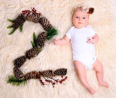 a baby laying on top of a white rug next to pine cones