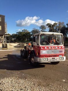 a red and white truck parked on top of a dirt field next to a building