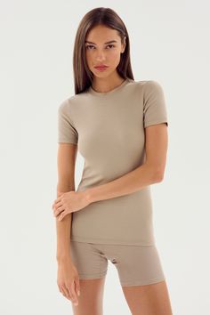 A woman with long brown hair, wearing the Louise Rib Short Sleeve in Latte by SPLITS59 along with matching shorts made from soft modal fabric, stands against a plain white background. Stretch Crew Neck Short Sleeve Top In Athleisure Style, Stretch Crew Neck Short Sleeve Top For Athleisure, Athleisure Stretch Crew Neck Short Sleeve Top, Fitted Short Sleeve T-shirt For Loungewear, Fitted Short Sleeve T-shirt For Yoga, Fitted Summer Top With Short Sleeves, Fitted Seamless T-shirt For Athleisure, Seamless Fitted T-shirt For Athleisure, Seamless Fitted Athleisure T-shirt