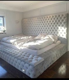 a large white bed sitting on top of a wooden floor next to a window in a bedroom