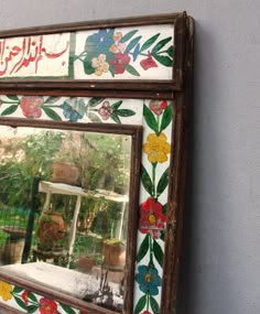 an ornately decorated mirror hanging on the wall in front of a building with flowers painted on it