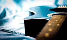 an acoustic guitar laying on a bed with blue sheets in the foreground and blurry background