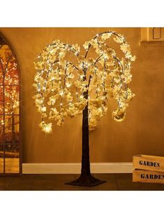 a lighted tree in the middle of a room next to a sign that says garden gardens