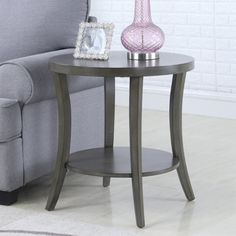 a small table with a pink vase on it next to a gray couch in a living room