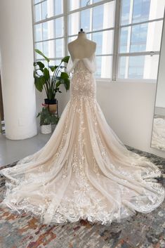 the back of a wedding dress on display in front of a window with potted plant