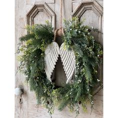 an angel wreath hanging on a door with pine cones and greenery in front of it