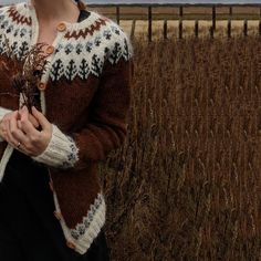 a woman standing in the middle of a field wearing a brown and white cardigan