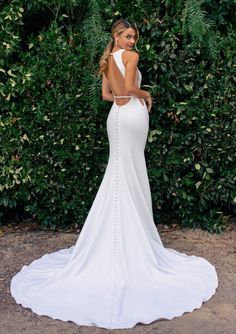 a woman wearing a white wedding dress standing in front of some bushes and greenery