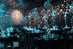 a room filled with tables covered in black and white table cloths topped with silver and blue balloons