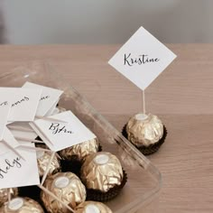 there are some chocolates in a plastic container on the table with name tags attached to them