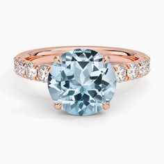 a rose gold engagement ring with an aqua blue topazte and white diamonds on the side