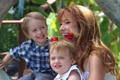 a woman sitting next to a little boy on top of a wooden bench with flowers in his hair