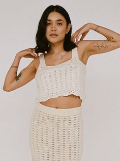 Sentence with replacement: Woman in a white Lyric Crochet Crop Tank - Ecru outfit, handmade in Peru, posing with hands raised slightly by her head. Crochet Crop Tank, Crochet Crop, Layered Look, Crop Tank, Summer 2024, The Label, Peru, Lay Flat, Crochet Top