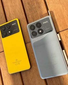 two cell phones sitting next to each other on a wooden table with one yellow and the other gray