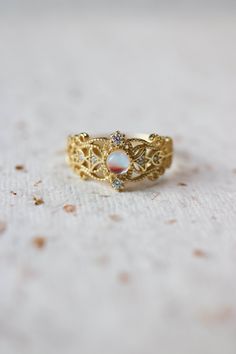 Sonia Moonstone Floral Gold Lace Filigree 18K Gold Vermeil Ring features moonstone in the centre, accented by lace filigree on the sides. It is similar to Monique Moonstone Ring in our shop, but the details of the ring are different. This is an adjustable ring, it comes in one size only and fits US ring size 5 to 8. ◊ 18K Gold Vermeil ◊ Adjustable Ring ◊ Sold in ONE SIZE only ◊ Fits US ring size 5 to 8 ◊ Lab Moonstone and cubic zircons ◊ Delivered in our signature royal blue box, it makes the pe Heirloom Gold Opal Gemstone Ring, Heirloom Gold Crystal Promise Ring, Delicate Gold Oval Opal Ring, Elegant Moon-shaped Opal Promise Ring, Elegant Moon Shaped Opal Promise Ring, Ethereal Yellow Gold Ring, Gold Round Mystical Moonstone Ring, Mystical Moonstone Moon-shaped Ring For Wedding, Mystical Moonstone Ring For Wedding