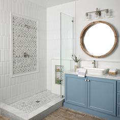 a white bathroom with blue cabinets and a round mirror