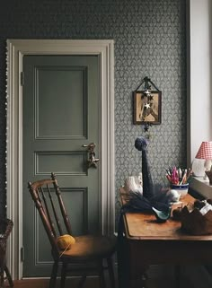 a room with a green door, chair and desk in front of the doorway to another room