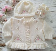 This hand knitted baby girls cardigan with matching hat & boots is the perfect little knitted sweater to keep your little ones warm, it matches perfectly with all your other baby clothes, jeans, leggings dresses.  This knitted outfit also makes a great gift for new moms or to give as a baby shower gift The cute baby sweater is hand knitted in soft acrylic baby yarn with a lovely lacy pattern to front & back the front is also hand embroidered with silk flowers  The Cardigan is finished with delic Fitted Cream Cute Sweater, Cute Fitted Cream Sweater, Cute Winter Knitting Pattern, Cute Winter Sweater As A Gift, Cute Fitted Knitted Cardigan, Cute Handmade Knitting Pattern For Winter, Handmade Cute Winter Knitting Pattern, Cute Handmade Winter Knitting Pattern, Cute Fitted Hand Knitted Sweater