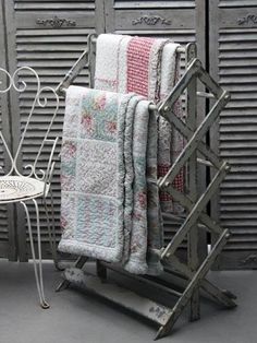 two towels are stacked on a rack next to an iron chair and side table in front of shutters