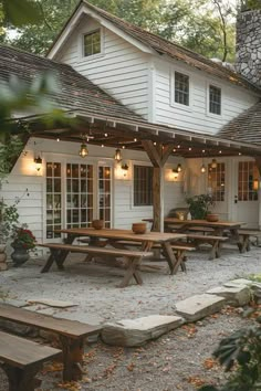 a white house with picnic tables and lights on the front porch, surrounded by trees