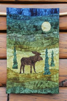 the moose is standing in front of the full moon on this quilted wall hanging