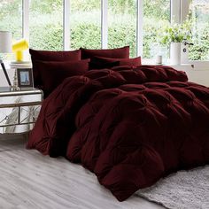 a bed with red comforter and pillows in front of large windows on the floor