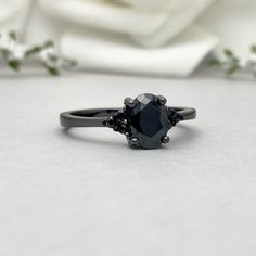 a black diamond ring sitting on top of a white flowered cloth with flowers in the background