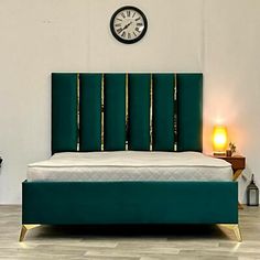 a bed with a green headboard sitting in a room next to a clock on the wall