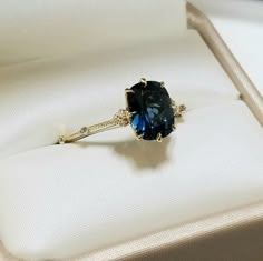 a ring with a blue stone in it sitting on a white cloth covered cushioned box