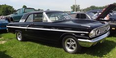 an old black car parked on top of a lush green field next to other cars