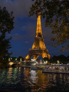 the eiffel tower lit up at night with boats on the river below it