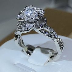 a white gold engagement ring with diamonds on the band and flower shaped center stone, set in 18k white gold