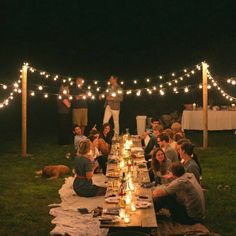 a group of people sitting around a long table with lights strung over it and food on the table