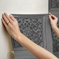 a woman is painting the wall with grey paint and she has her hands on it