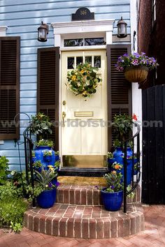 a blue house with shutters and flowers on the front door, steps leading up to it