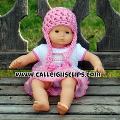 a doll sitting on a wooden bench wearing a pink crocheted hat and dress