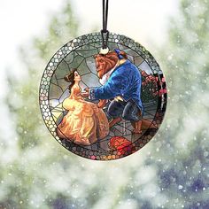 a stained glass ornament with a beauty and the beast scene hanging from it