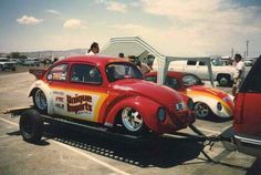 an old red car is being towed by a flatbed tow truck in a parking lot