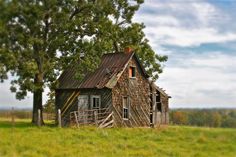 an old run down house sitting in the middle of a field next to a tree