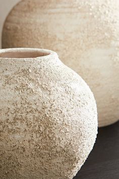 two white vases sitting side by side on a black counter top, one is made out of concrete