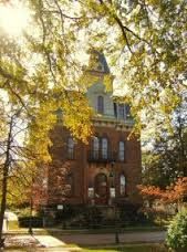 an old brick building surrounded by trees in the fall time with leaves on the ground