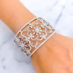 This exquisite 18k white gold bangle bracelet, weighing 63.1 grams, features an extravagant floral motif adorned with dazzling diamonds. The white gold finish enhances its luxurious appeal, making it perfect for any special occasion. The bangle is set with 8.43 carats of F-G color, VS quality diamonds in round and marquise shapes. With an oval opening of 2.4 inches, this cuff bangle with side hinges offers both elegance and comfort. Ideal for those who appreciate high-quality craftsmanship and t Glamorous Diamond Bangle Bracelet, Party Diamond Bracelet In White Gold, Fine Jewelry White Gold Bracelets With Intricate Design, White Gold Bracelets With Intricate Design For Fine Jewelry, White Gold Bracelets With Intricate Design, Fine Jewelry White Gold Cuff Bracelet With Cubic Zirconia, Glamorous Diamond Bracelet With Accents For Formal Events, White Gold Cubic Zirconia Cuff Bracelet, Glamorous Diamond Bracelet For Gift