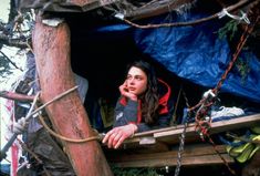 a woman sitting on top of a wooden boat next to a blue tarp covered tree