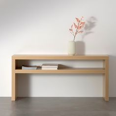 a vase with a plant on top of a wooden shelf next to a white wall