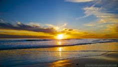 the sun is setting over the ocean with clouds in the sky and water on the beach