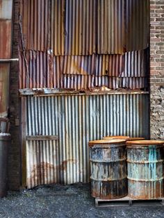 an old rusty building with several barrels next to it