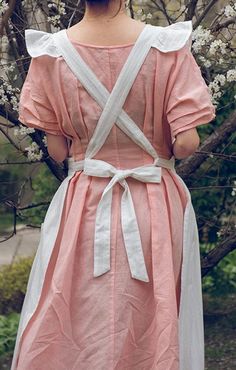 a woman wearing a pink dress standing in front of a tree with white flowers on it