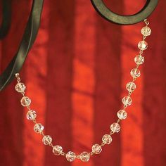 a close up of a necklace hanging from a metal hook on a red wall with a curtain in the background